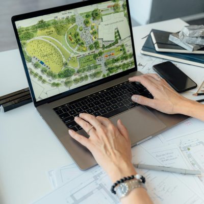 Architect working on landscape plan displayed on laptop with hands typing on keyboard.